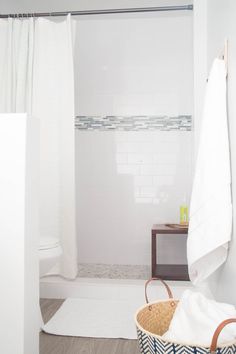 a white bathroom with a basket and towel on the shower door sill next to it