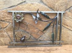 a metal frame with flowers and birds on it next to a stone wall in the shape of a rectangle