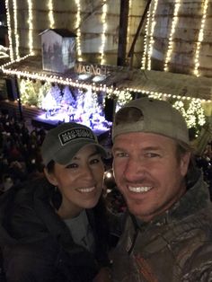 a man and woman posing for a photo in front of a building with christmas lights