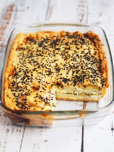 a casserole dish with cheese and black sprinkles in it on a wooden table