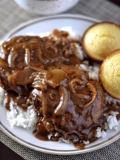 a white plate topped with rice and meat covered in gravy on top of a table