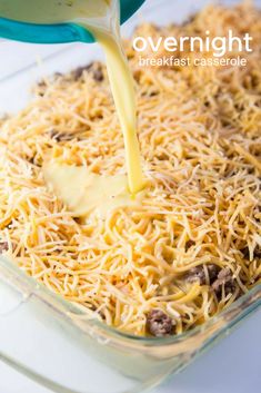 someone pouring cheese into a casserole in a glass dish on a white table