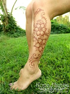 a woman's legs with tattoos on them sitting in the middle of some grass