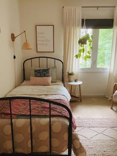 a bed room with a neatly made bed next to a window and a lamp on the wall