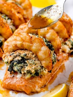 a spoon is being drizzled with sauce on top of baked shrimp and spinach