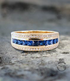 a gold ring with blue sapphires and white diamonds on the outside, sitting on top of a rock