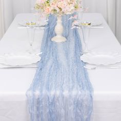 a white table topped with a vase filled with flowers next to two glasses and plates