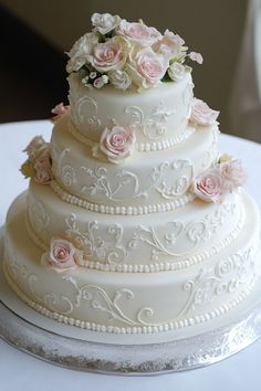 Elegant four-tier white wedding cake adorned with delicate pink roses and intricate icing designs. White And Peach Wedding Cake, 1960s Wedding Cake, Wedding Cake With Frosting Flowers, Cute Simple Cake Designs, Vintage Style Wedding Cake, Wedding Cakes Pink, Trendy Wedding Cake, Wedding Cakes Unique, Wedding Cake Vintage