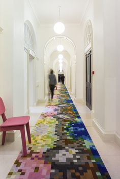 a long hallway with colorful rugs on the floor and two people walking down it