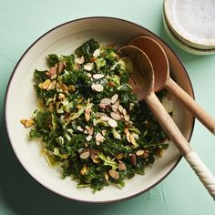 a bowl filled with greens and nuts on top of a blue tablecloth next to two wooden spoons