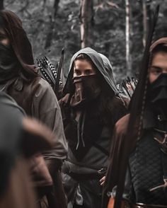 a group of people dressed in medieval clothing and holding spears, with trees in the background