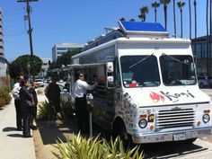 people are standing in line to get food from the food truck that is parked on the side of the road