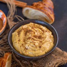 a bowl of hummus sitting on top of a table next to bread and cinnamon sticks