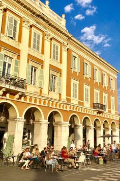 people sitting at tables in front of an old building with columns and balconies