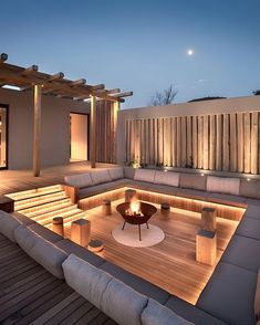 an outdoor seating area lit up at night with lights on the benches and fire pit