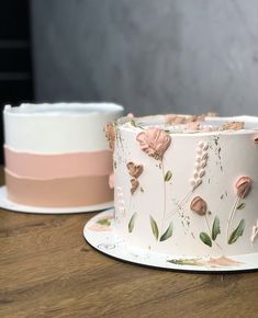 two cakes decorated with pink and white frosting on top of a wooden table next to each other