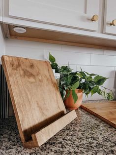 a wooden cutting board sitting on top of a counter next to a potted plant