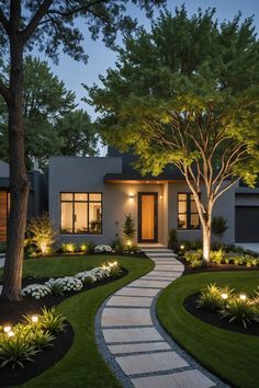 a modern house with landscaping and trees in the front yard at night, lit up by outdoor lighting