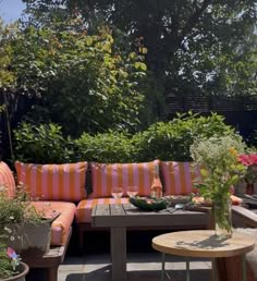 an outdoor seating area with potted plants and flowers on the table, surrounded by greenery