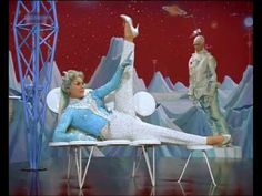 a woman laying on top of a white chair next to two men in space suits