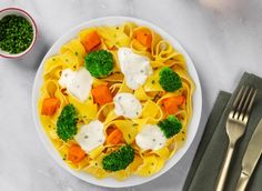 a white plate topped with pasta covered in cheese and veggies next to silverware