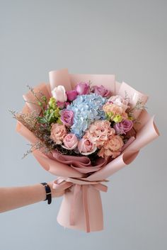 a woman holding a bouquet of flowers in her hand with pink and blue blooms on it