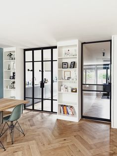 a dining room table with chairs and bookshelves in front of glass doors that lead to an open living area