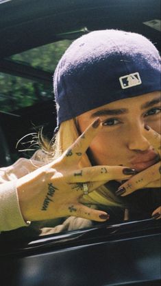 a woman with her hand on the steering wheel of a car while wearing a beanie