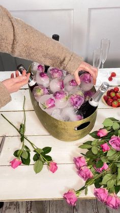 a woman is pouring ice into a bucket filled with flowers and wine glasses on a table