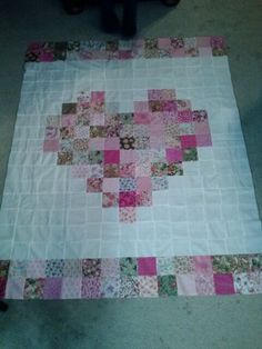 a pink and white patchwork quilt on the floor next to a person sitting in a chair