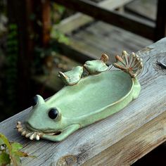 a green frog figurine sitting on top of a wooden bench with two little birds perched on it's back