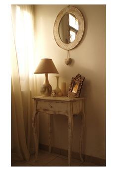 a small table with a lamp and mirror on it next to a window sill