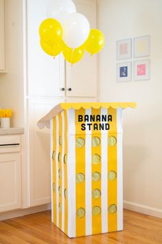 a banana stand with balloons in the background and a box on the floor next to it