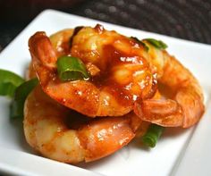 a white plate topped with shrimp covered in sauce and garnished with green leaves