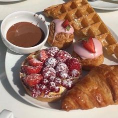 a white plate topped with waffles, strawberries and pastries next to chocolate