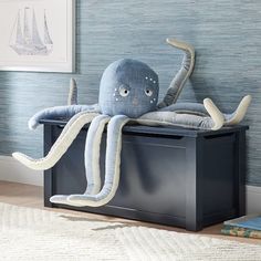 an octopus stuffed animal sitting on top of a black box next to a blue wall