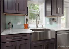 a kitchen with gray cabinets and white counter tops, stainless steel dishwasher and sink