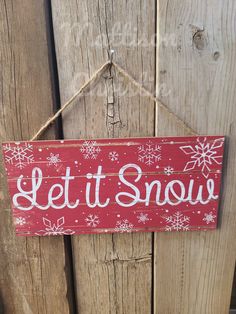 a sign that says let it snow hanging on a wooden fence with snowflakes