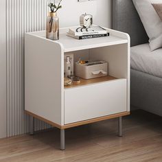 a white nightstand with flowers and books on it next to a gray couch in a living room