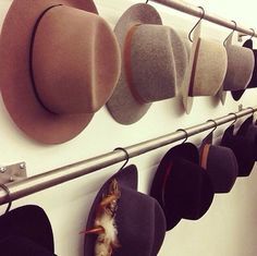 several hats are hanging on a wall with metal bar and hat hangers attached to it