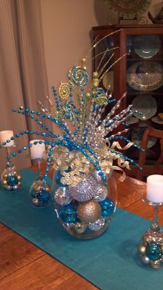 a vase filled with blue and silver ornaments sitting on top of a table next to candles