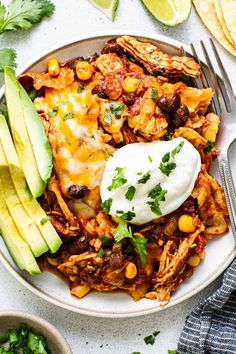 a white plate topped with mexican food next to avocado wedges and cilantro