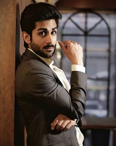 a man in a suit leaning against a wall with his hand on his chin and looking at the camera