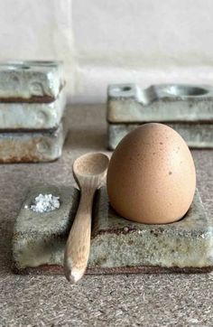 an egg sitting on top of a stone block next to two spoons and salt shakers