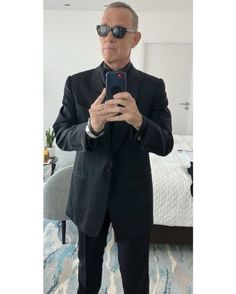 a man in a suit and sunglasses taking a selfie with his cell phone while standing on a bed