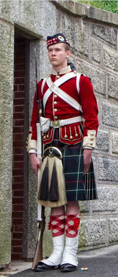 a man in a kilt standing next to a brick wall with a pipe and bagpipe