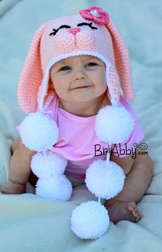 a baby girl wearing a bunny hat with pom poms