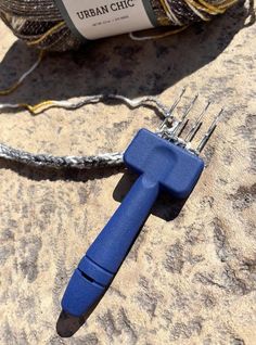 a blue handled wrench sitting on top of a rock next to a ball of yarn