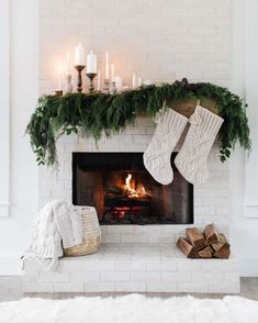 a white fireplace with stockings and candles on it, surrounded by greenery in front of the fire