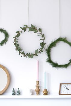 three wreaths are hanging on the wall above a mantle with candles and other decorations